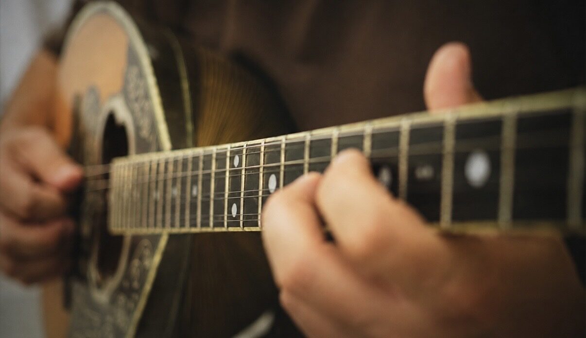 Close-up of both hands playing a bouzouki, fretting hand on the neck
